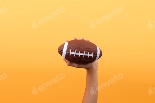 Preview: Hand Holding American Football Against Yellow Background