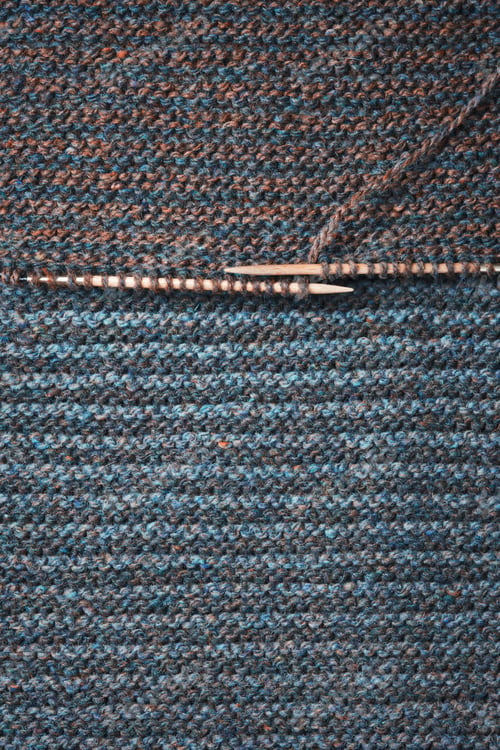 Preview: Striped knitted fabric and wooden needles. Dark knitted texture background.