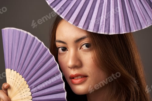 Preview: Cropped portrait of an attractive young woman posing with fans in studio against a grey background