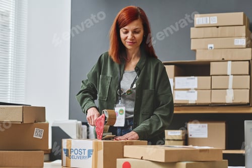 Preview: Young female volunteer sealing cardboard box with clothes with cellotape