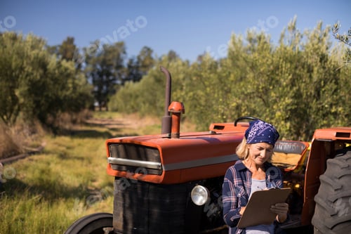 Preview: Woman leaning on tractor while writing on clipboard