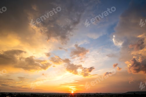 Preview: Dramatic sunset landscape with puffy clouds lit by orange setting sun and blue sky