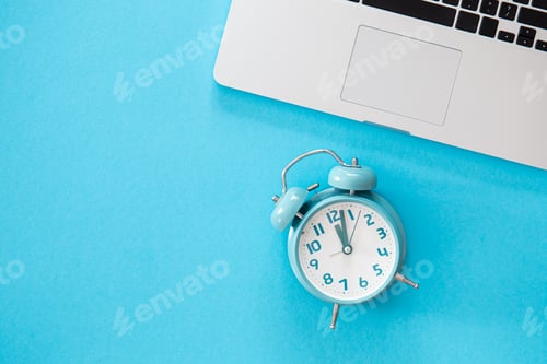 Preview: Alarm clock and laptop on a blue background, flat lay.