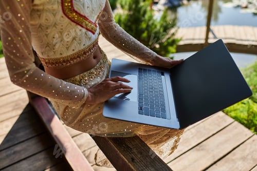 Preview: cropped view of indian woman in traditional clothes networking, using laptop in summer park
