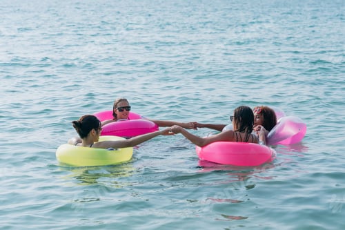 Preview: Teenagers laughing and playing in the sea with colorful swim rings, enjoying youthful summer fun.
