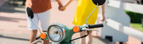Preview: partial view of blurred multiethnic couple holding hands near scooter, banner