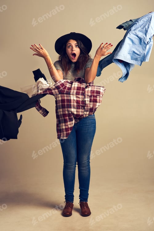 Preview: Fashion frenzy. Studio shot of a young woman tossing clothing against a brown background.