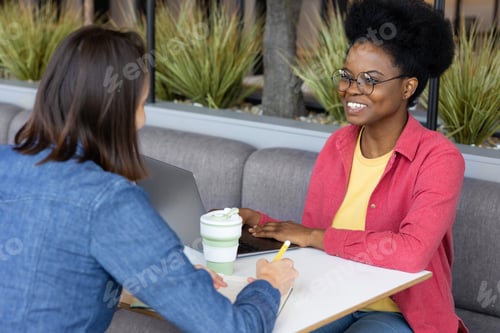 Preview: Young and pretty African American woman chatting with friend or colleague in coffee shop