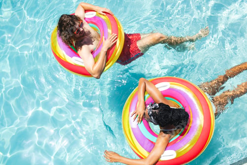 Preview: A diverse couple, a young Caucasian man and an African American woman relax on colorful pool floats