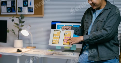 Preview: Asian ui designer is comparing two different versions of a mockup for a mobile phone app while worki