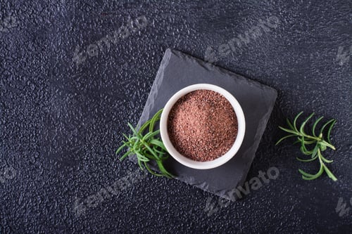 Vista previa: Black Himalayan kala namak salt in a bowl and rosemary on a black background. Top view.