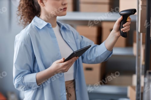 Preview: Close-up of young woman in blue shirt scanning qr codes on packed boxes