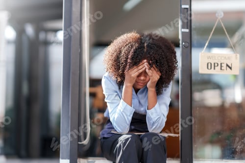 Preview: Female shopkeeper sitting stressed out at the store entrance frustrated by the economic impact.