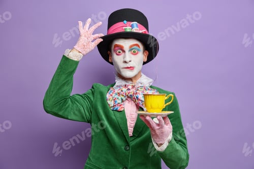 Preview: Time for having tea. Aristocratic gentleman with bright makeup has image of fictional character hold
