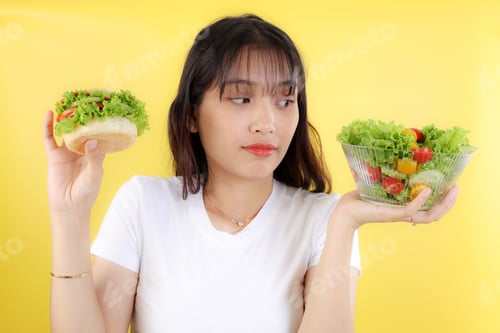 Preview: Young Asian Woman Choose Healthy Salad or Burger Junkfood with Unhappy Face.