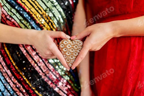 Preview: Two women are holding heart shape cookie in a Valentine's Day party
