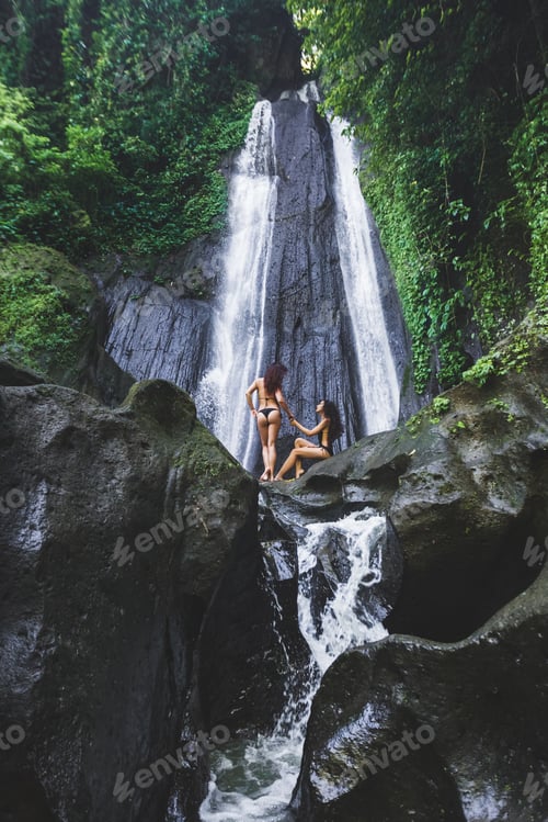 Preview: Two slim women relaxing near beautiful waterfall in Bali jungle. Nature adventure Dusun Kuning