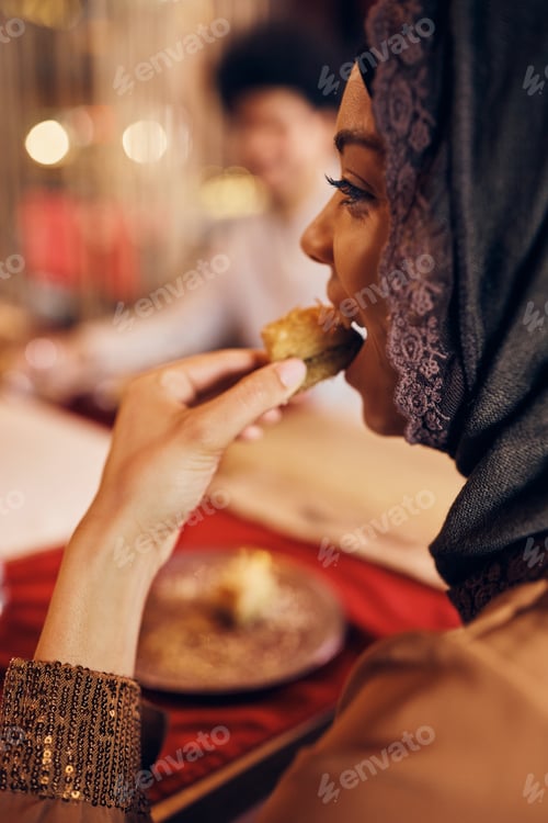Preview: Young Muslim woman eating baklava for dessert.