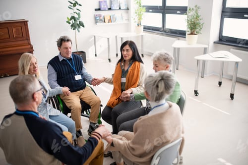 Preview: Group of senior people sitting in circle during therapy session, holding hands and praying together