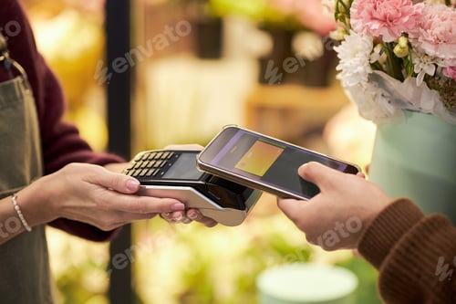 Preview: Caucasian Young Adult Paying with Smartphone near Flowers at Checkout Counter