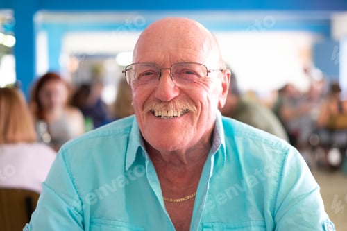 Preview: Portrait of attractive happy senior man sitting at a restaurant table looking at camera