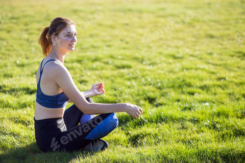 Preview: Young sportive woman in yoga position meditates in field at sunrise.