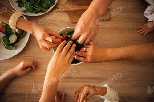 Preview: Diverse hands of adults and children reaching for fresh salad ingredients in a bowl