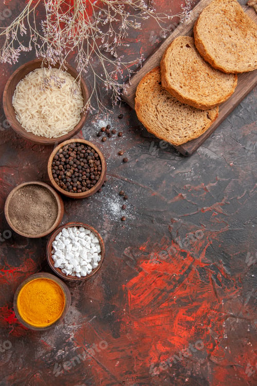 Preview: top view bread slices on cutting board bowls with rice black pepper sea salt turmeric on dark red