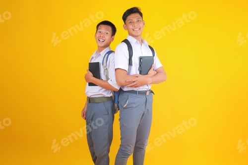 Preview: Cheerful Students Pose Back to Back With Notebooks in Vibrant Yellow Studio Portrait