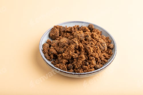 Preview: plate with unrefined cane sugar on orange pastel. side view, close up.