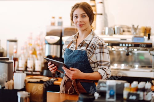 Preview: Portrait of smiling cafe owner using a digital tablet behind the bar counter in modern coffee shop.