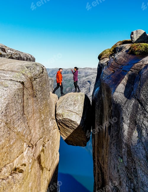 Preview: Kjeragbolten, Norway, Two people stand on a rock bridge overlooking a stunning Norwegian landscape