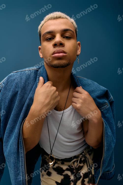 Preview: Stylish young man with dyed hair wearing denim jacket against a blue background