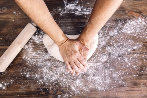 Preview: hands of a person kneading bread on a wooden table