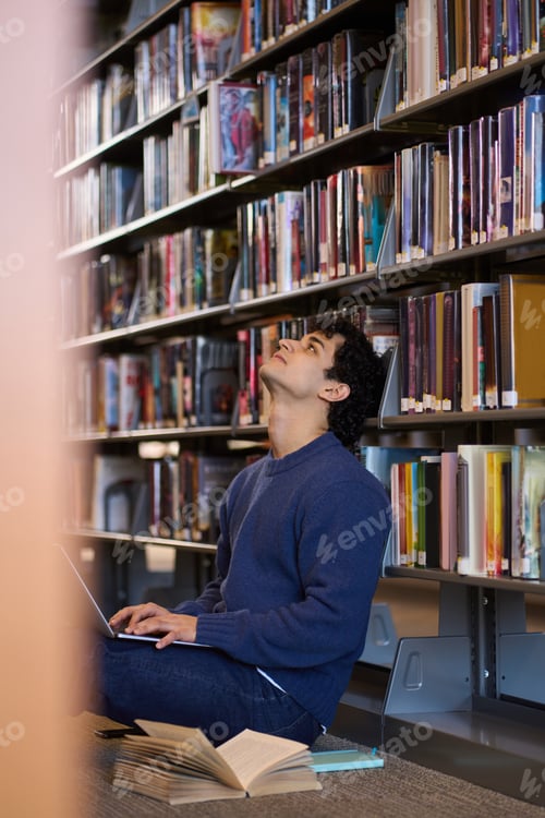 Preview: Multitasking man student, using laptop for study, sitting on the floor in university library campus