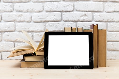 Preview: Tablet rests beside open book on wooden table against a white brick wall backdrop