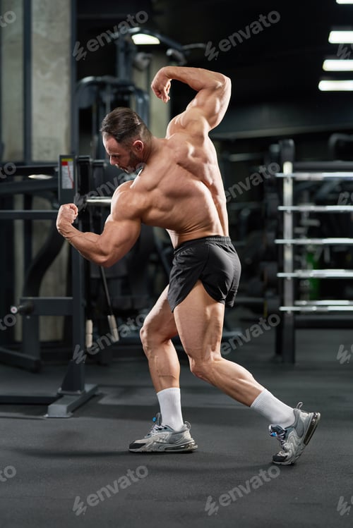 Preview: Muscular male model bending body, tensing muscles in gym.