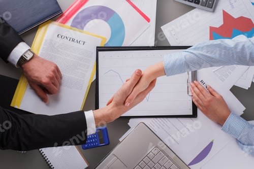 Preview: Man and woman shaking hands over table with financial graphics.