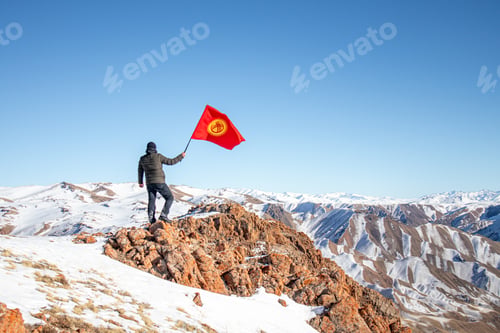 Preview: Man holds a Kyrgyzstan flag on a snowy mountain peak