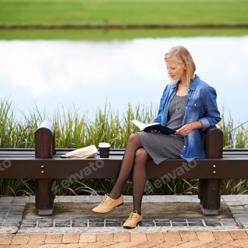 Preview: Shot of an attractive blonde woman reading a book during her lunch break on a park bench