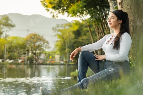 Preview: beautiful latin girl sitting by the lake admiring the golden sunset, while thinking about her future