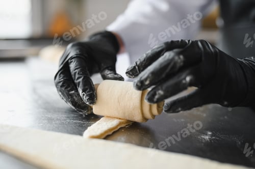 Preview: Baker rolling dough for croissant in bakery kitchen