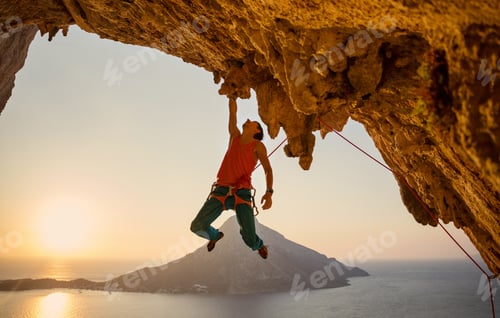 Preview: Male rock climber hanging with one hand on challenging route on cliff