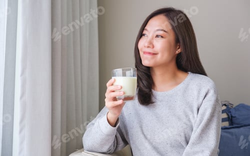 Preview: Portrait image of a young woman holding and showing a glass of fresh milk