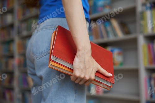 Preview: Closeup view female hands holding pair of books over bookshelves on background