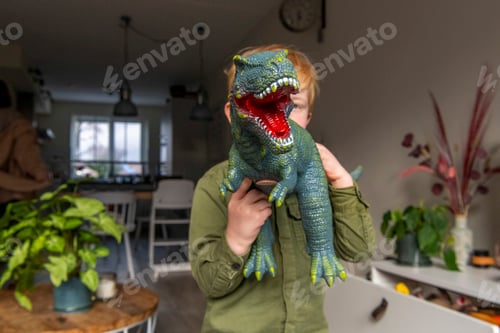 Preview: Child playfully poses with a toy dinosaur covering their face