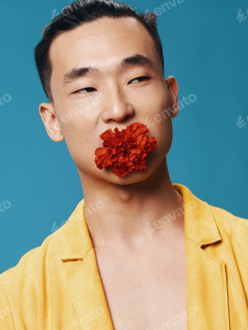 Preview: Happy male of Korean appearance on a blue background with a flower in his mouth