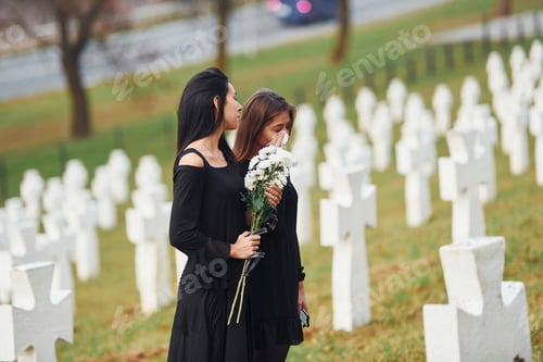 Preview: Two young women in black clothes visiting cemetery with many white crosses