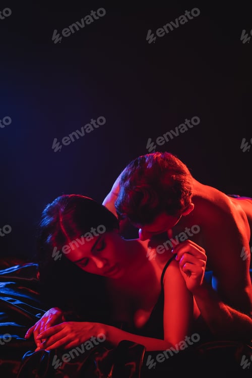 Preview: young shirtless man hugging sexy woman in red lighting on black background