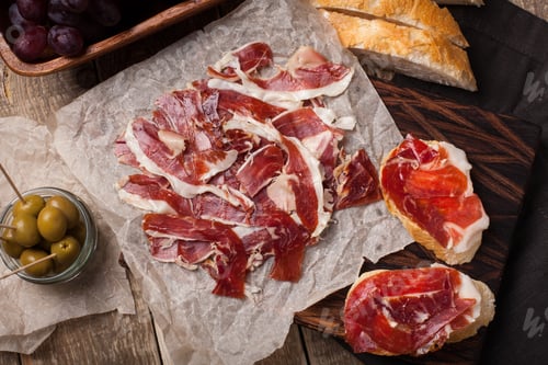 Preview: Jamon Iberico with white bread, olives on toothpicks and fruit on a wooden background. Top view